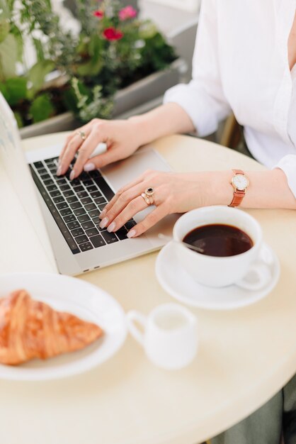Mãos de uma mulher com café e laptop em um café ao ar livre no verão