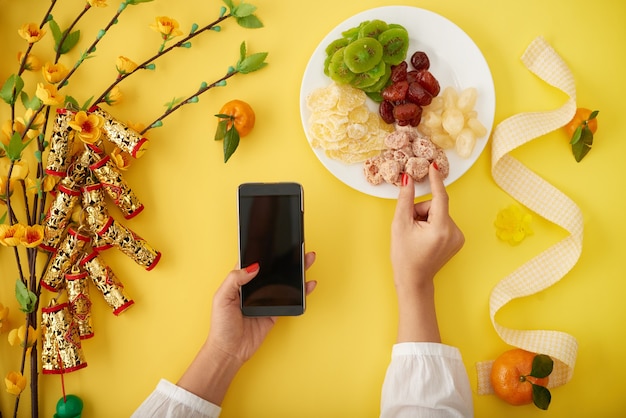 Mãos de uma mulher comendo lanches tradicionais do ano novo chinês e enviando mensagens de texto de saudação para seus amigos e familiares via smartphone