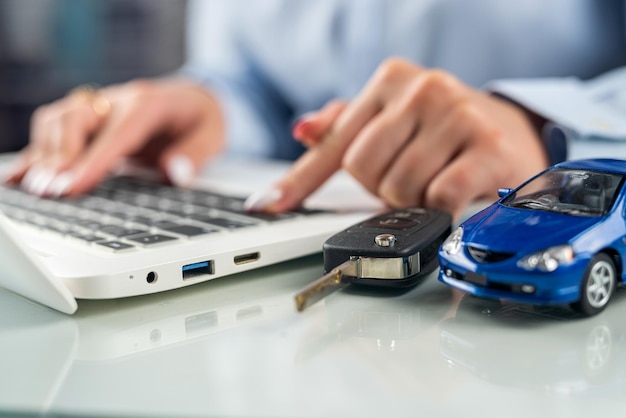 Mãos de uma mulher em uma mesa atrás de um teclado com um pequeno modelo de carro