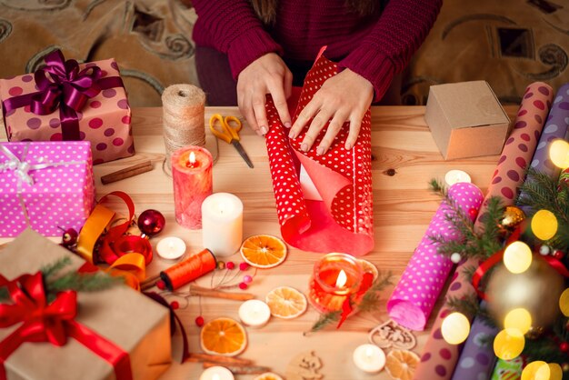 Mãos de uma mulher embrulhando um presente de natal em uma mesa de madeira