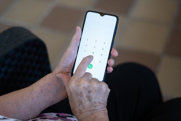 Mãos de uma mulher idosa com um telefone celular para fazer uma ligação para um idoso e novas tecnologias