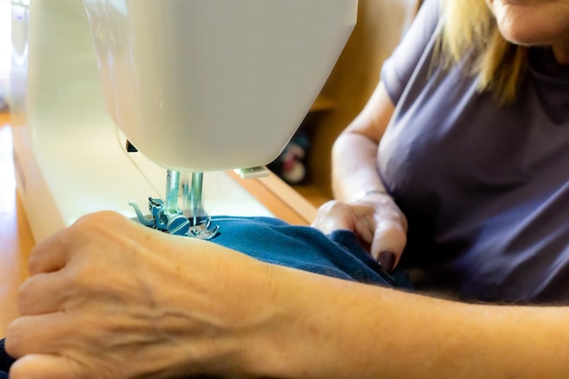 Mãos de uma mulher irreconhecível colocando a agulha e a roupa para costurar com sua máquina