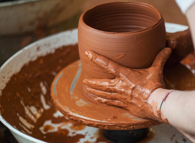 Foto mãos de uma mulher oleira moldando um pedaço de barro na roda do oleiro