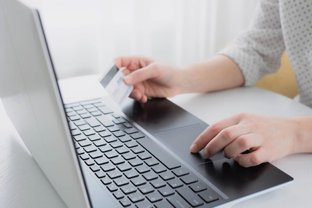 Mãos de uma mulher segurando um cartão de crédito e usando o computador laptop em casa. Conceito de compra online