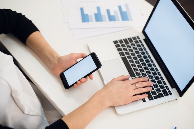 Mãos de uma mulher usando um telefone e um laptop