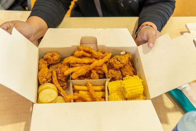 Foto mãos de uma pessoa irrecognizável abrindo uma caixa de fast food com milho de frango e batatas fritas