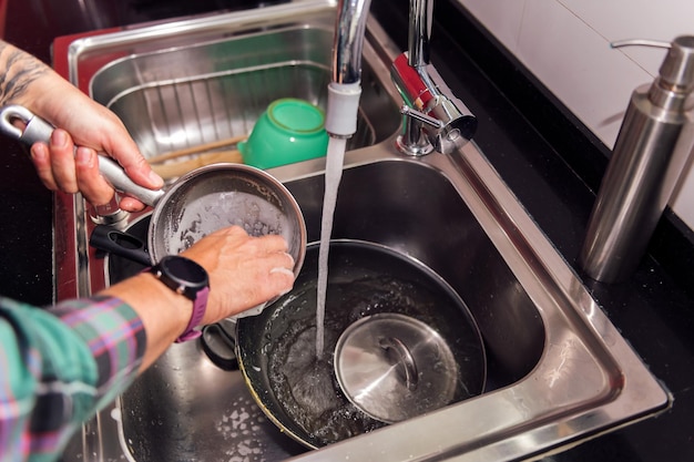 Mãos de uma pessoa limpando pratos e panelas