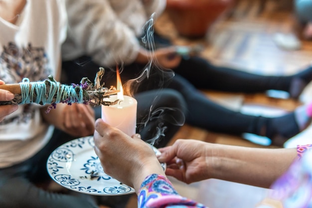 Mãos de uma xamã feminina com uma vela acendendo um feixe de canela em uma cerimônia de cura