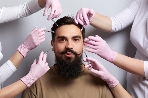 Mãos de vários médicos segurando seringas sobre o rosto masculino beleza e cosmetologia conceito cosmético