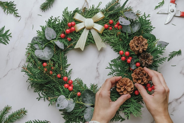 Mãos decorando guirlanda de natal artesanal com pinhas