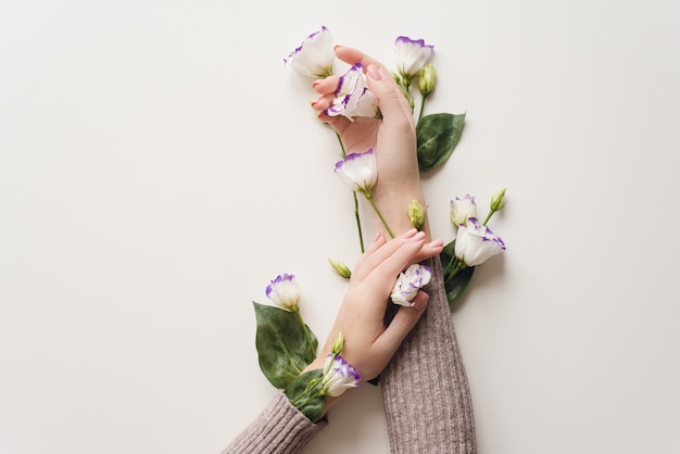 Mãos delicadas e flores da primavera de eustoma estão sobre a mesa branca.