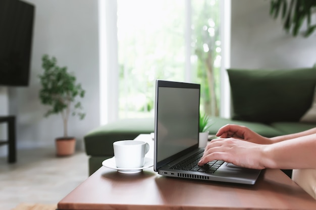 Mãos digitando no notebook cinza. Tela em branco vazia na mesa de centro de madeira. Apartamentos elegantes