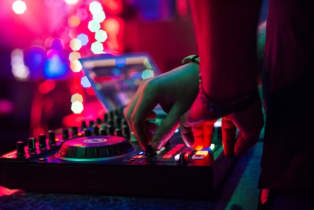 Mãos DJ tocando e mixando músicas no controlador de música em uma festa