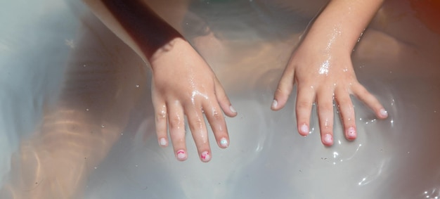 Mãos do bebê na água na piscina inflável
