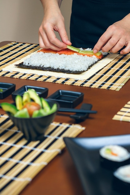 Mãos do chef colocando ingredientes no arroz para fazer sushi