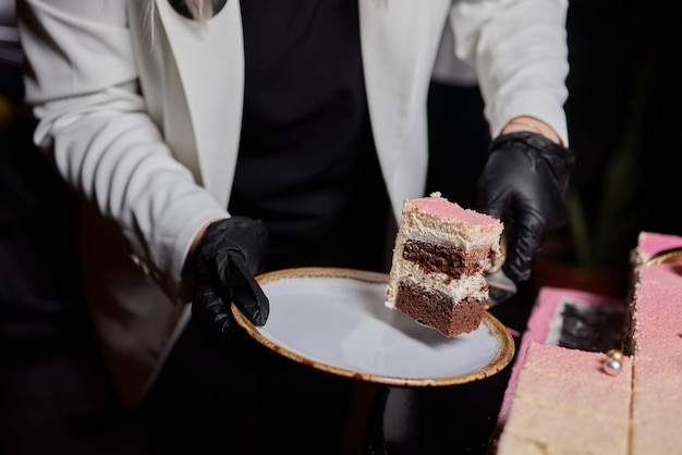 Mãos do chef em luvas de látex pretas cortando bolo de chocolate
