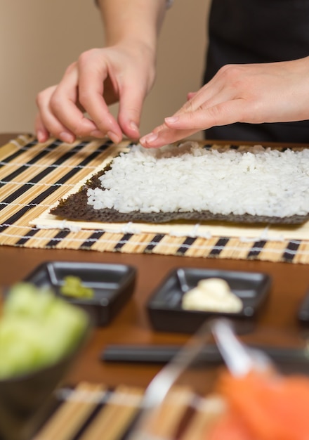 Mãos do chef mulher enchendo rolos de sushi japonês com arroz em uma folha de alga nori. Foco seletivo em sushi roll.