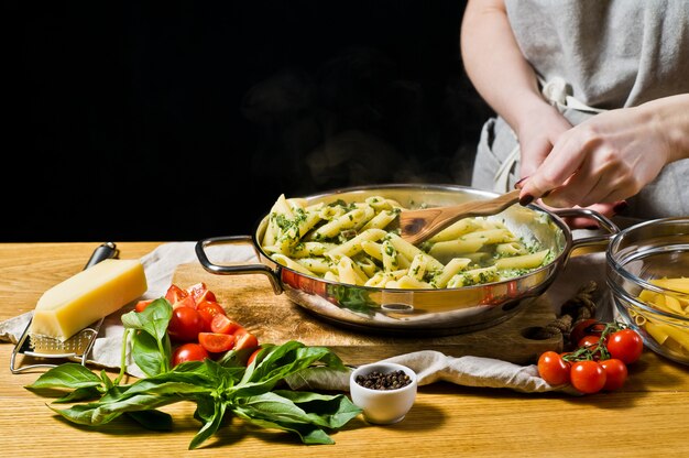 Mãos do cozinheiro chefe que preparam a massa de Penne com espinafre.