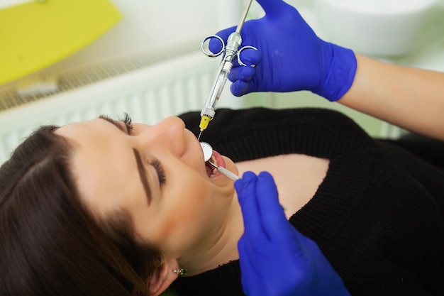 Mãos do dentista segurando a ferramenta e seringa nas mãos