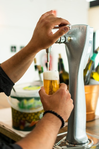 Mãos do empregado de bar na torneira da cerveja que derrama uma cerveja de lager do esboço que serve em um restaurante ou em um bar.