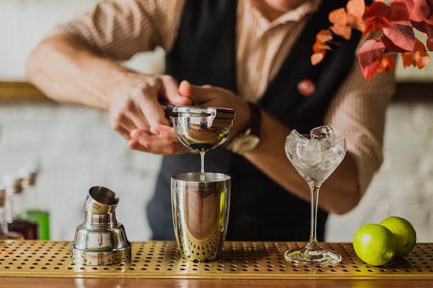 mãos do homem espremendo suco de limão em uma coqueteleira no bar. Foco seletivo, luz natural.