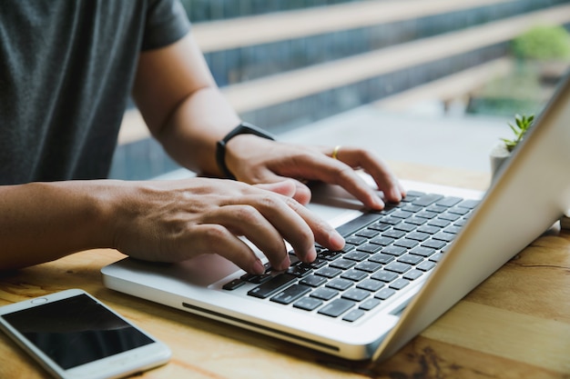 Mãos do homem ocupado trabalhando em seu laptop sentado na mesa de madeira