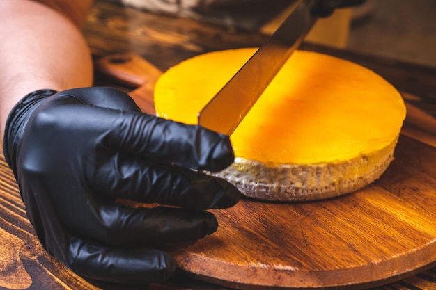 Mãos do jovem chef padeiro cortando fatia de cheesecake de manga