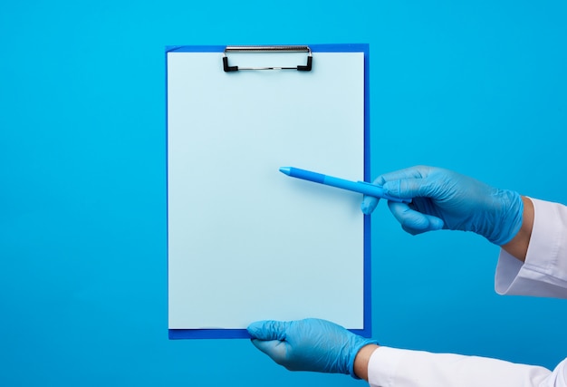 Mãos do médico feminino em luvas azuis de látex médica detém uma pasta com um clipe de papel e uma caneta de plástico