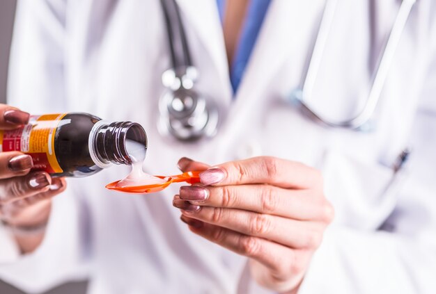 Mãos do médico jovem derramando xarope medicinal na colher.