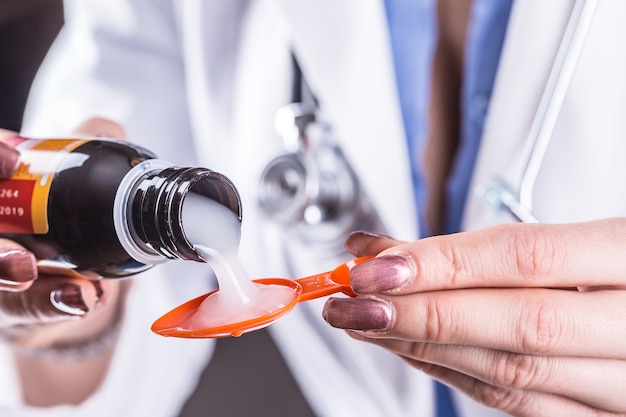 Mãos do médico jovem derramando xarope medicinal na colher.