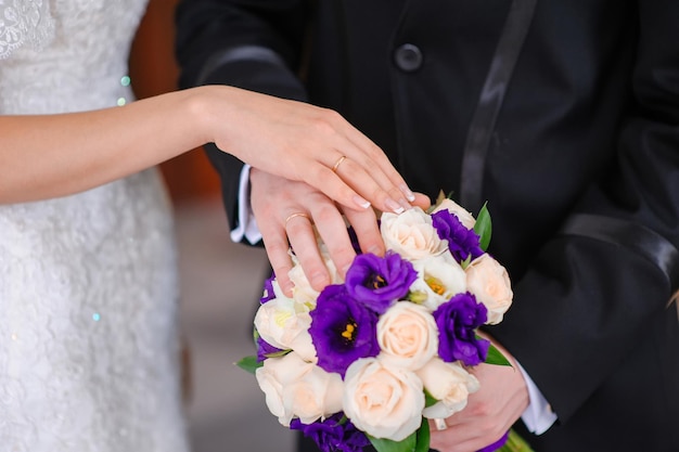 Mãos do noivo e da noiva no buquê de casamento