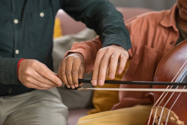 Mãos do professor de música e seu aluno tocando violoncelo, enquanto o jovem segurando violino e ajudando o menino a deslizá-lo