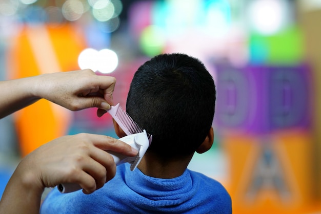 Foto mãos do rapaz pequeno do cabelo do corte do cabeleireiro que usa o pente e a tosquiadeira no barbeiro bonito.