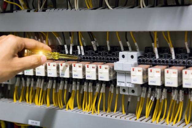 Mãos dos eletricistas que testam atual elétrico no painel de controle.