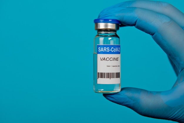 Mãos em luvas azuis segurando o frasco da vacina contra o coronavírus covid-19. fechar-se.