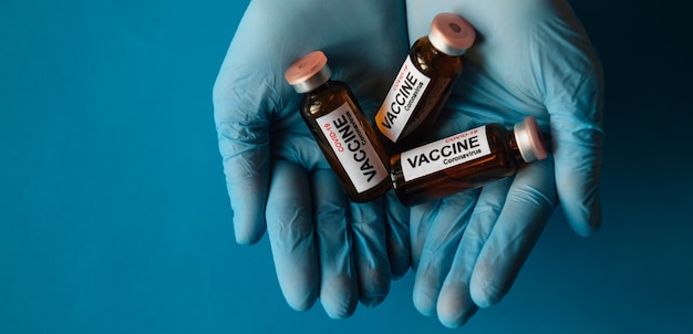Mãos em luvas de látex segurando frascos da nova vacina de coronavírus, close-up sobre fundo azul. Médicos e cientistas contra a pandemia covid-19. Medicamento pronto para testar em voluntários. Copie o espaço.