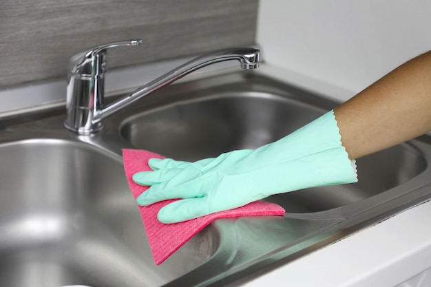 Mãos em luvas de proteção com pano para limpar a pia. empregada doméstica ou dona de casa limpa a casa. limpeza geral ou lavagem regular.