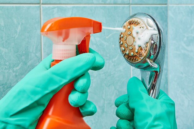 Mãos em luvas de proteção de borracha verde, lavam o chuveiro com ajuda de spray de limpeza.