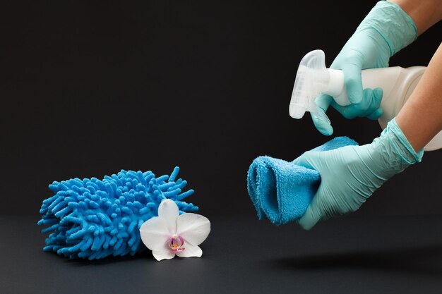 Mãos em luvas segurando uma garrafa plástica de líquido de lavagem e um capacho, um pano e uma flor de orquídea