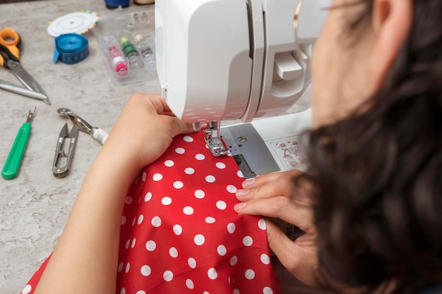 Mãos em mulher latina atraente usando máquina de costura mais fios de tesoura tecido fazendo roupas