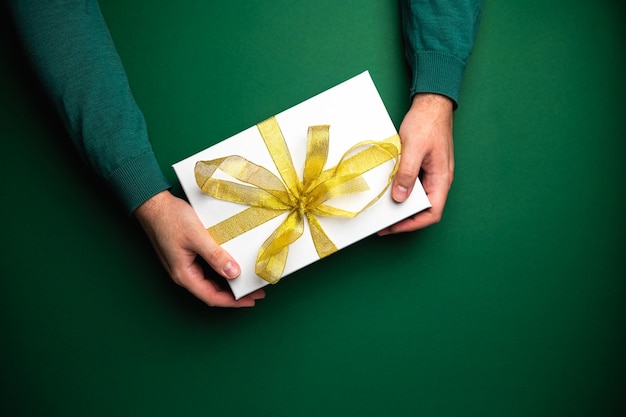 Mãos em suéter aconchegante seguram linda caixa de presentes de natal presente com fita dourada de fundo verde