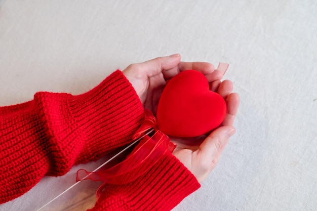 Mãos em um suéter vermelho segurando um coração vermelho com fitas