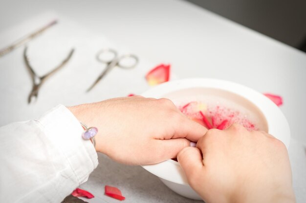 Mãos em uma tigela branca banham as unhas com água e pétalas de rosa para amaciar a cutícula e secar a pele