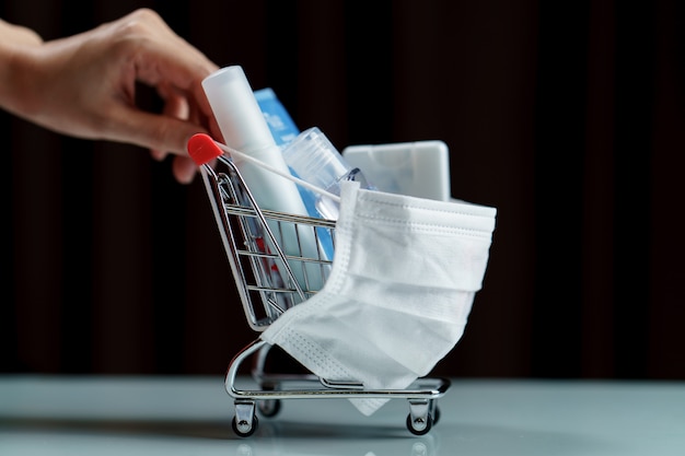 Mãos empurrando produtos de carrinho e desinfetantes com máscara protetora contra vírus corona ou proteção Covid-19.