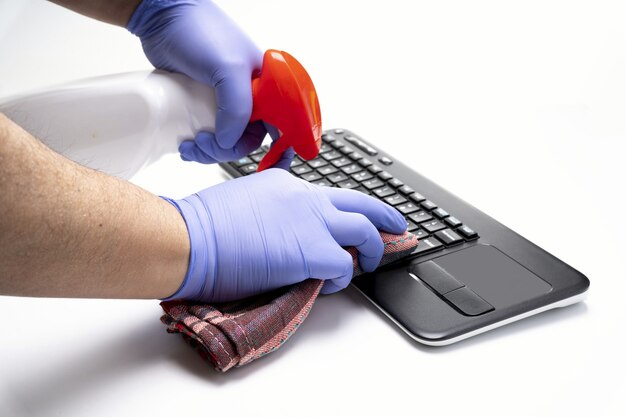 Mãos enluvadas limpando teclado de computador em fundo branco