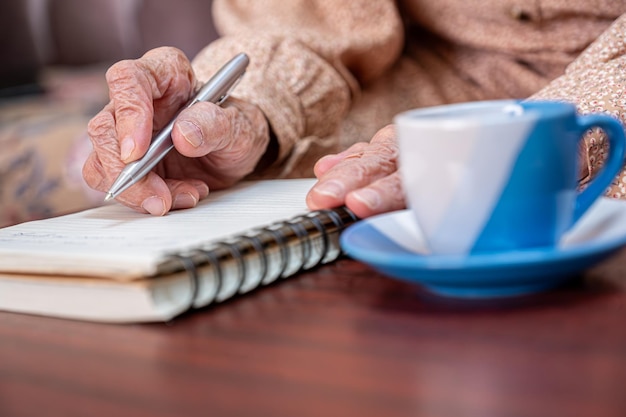 mãos enrugadas para um idoso escrevendo notas em seu caderno enquanto toma café