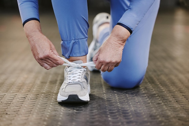 Mãos esportivas e sapatos de amarrar na academia para iniciar o treinamento ou exercício para o bem-estar Saúde do atleta de fitness ou mulher sênior amarrando tênis ou cadarços de calçados para se preparar para se exercitar ou correr