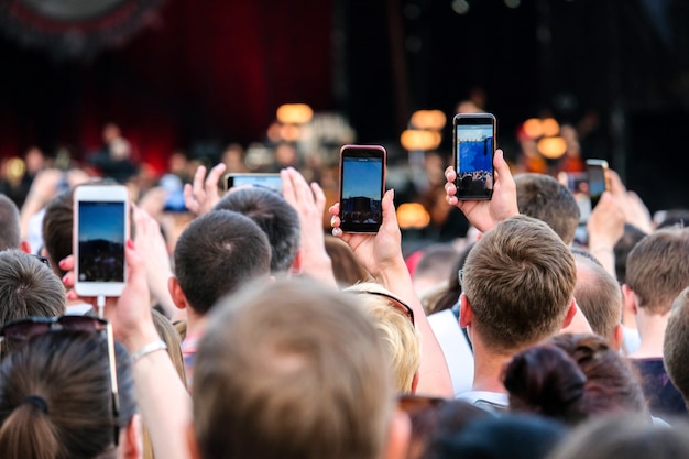 Mãos estendidas levantadas com os smartphones que fotografam a fase na multidão durante um concerto.