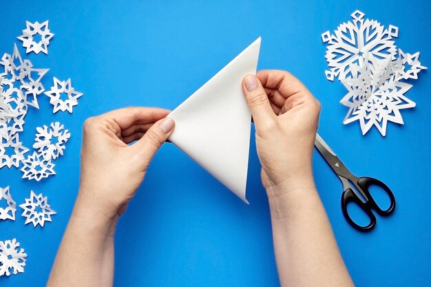 Mãos fazendo flocos de neve de papel branco em azul