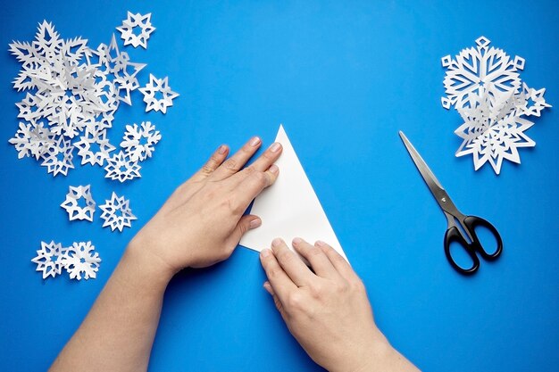 Mãos fazendo flocos de neve de papel branco em azul